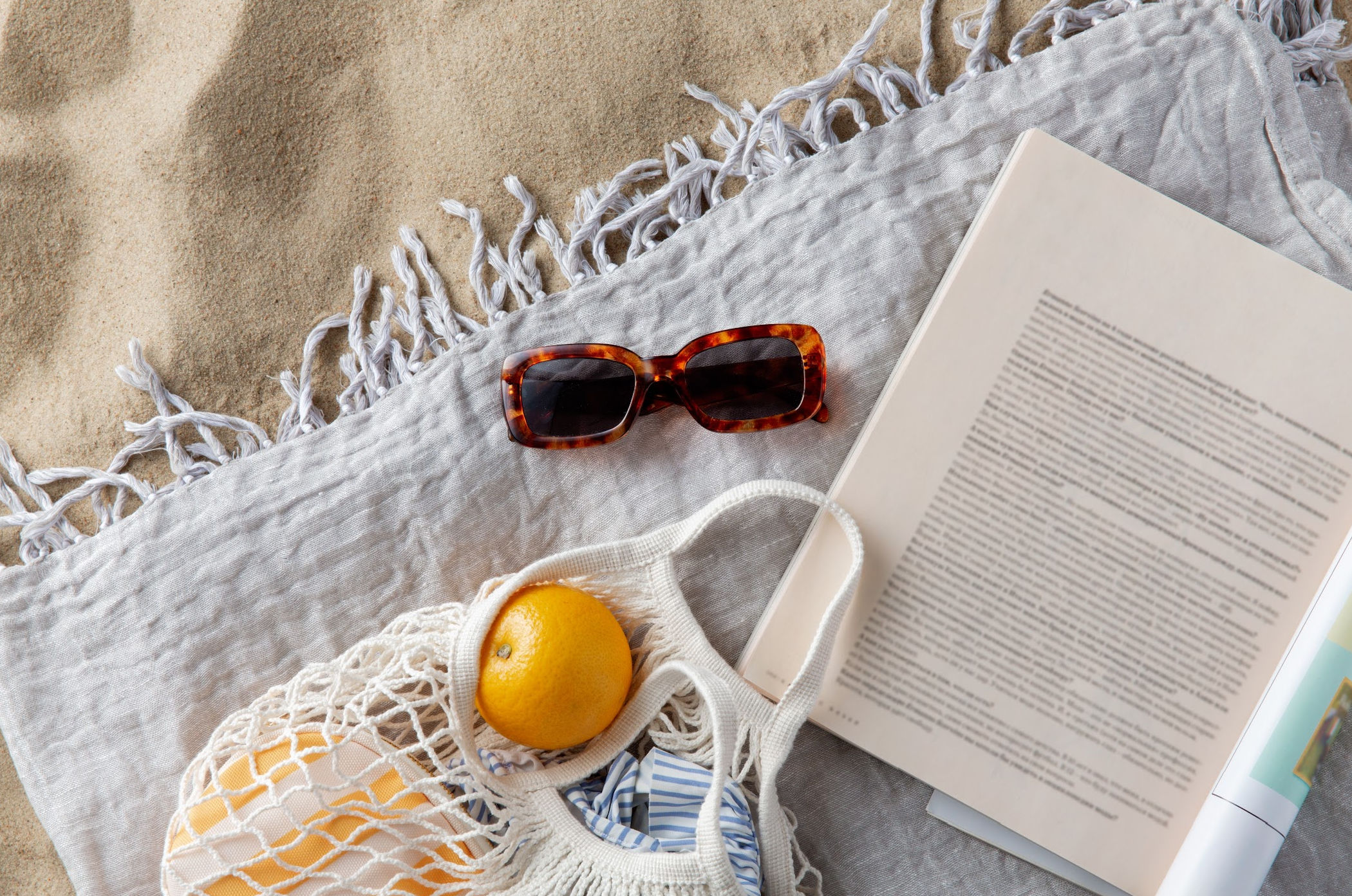 Book, sunglasses, and beach towel on sand for summer reading
