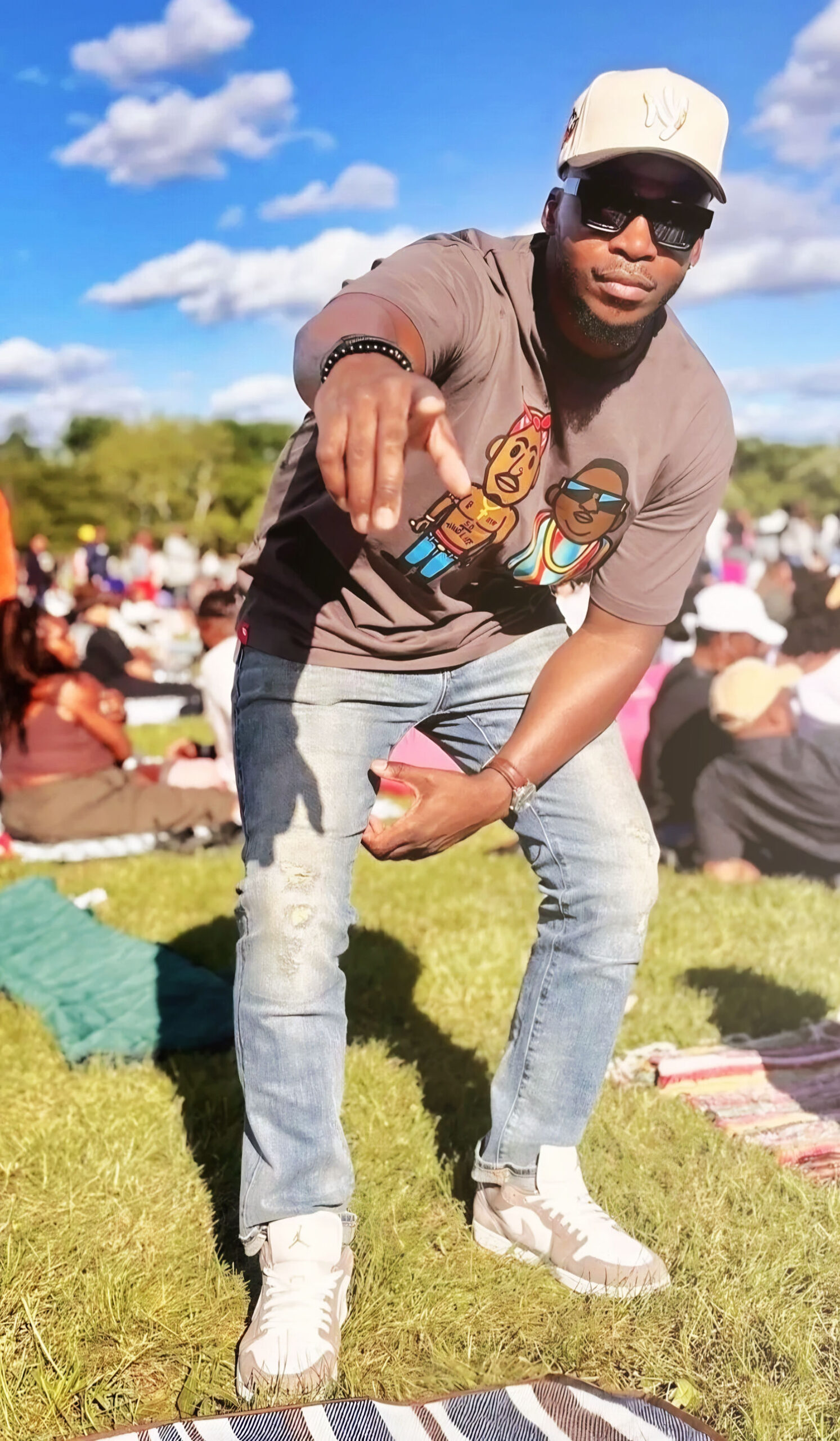 Roots Picnic fashion featuring a charcoal graphic T-shirt, light-wash denim, Yankees cap, sunglasses, and neutral sneakers.