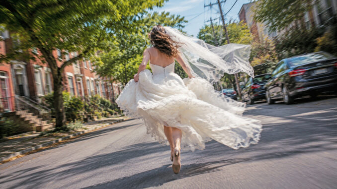 Runaway bride in a flowing wedding dress racing down a Philadelphia street