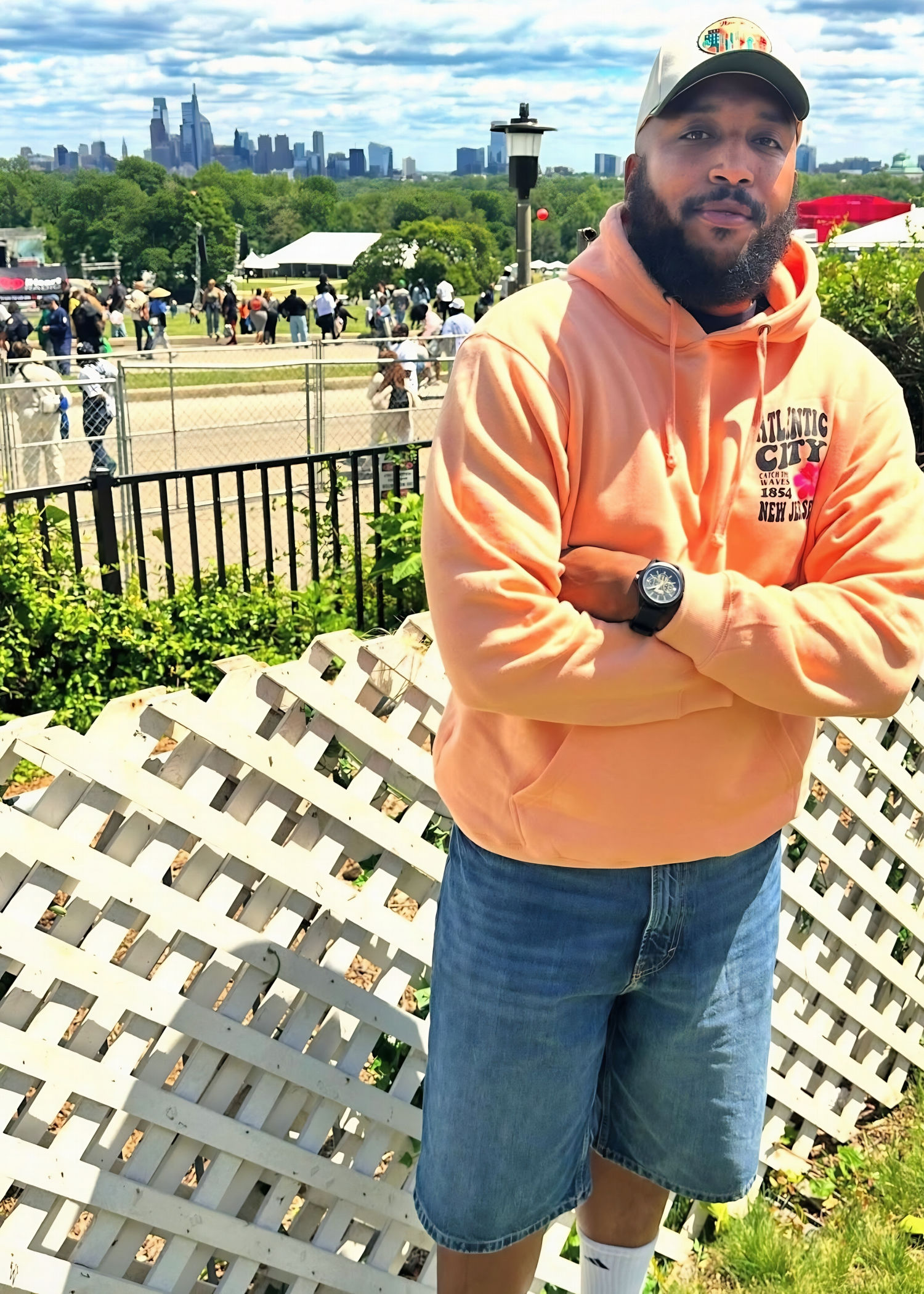 Roots Picnic fashion featuring a coral hoodie, jean shorts, and casual festival streetwear with the Philadelphia skyline in the background.
