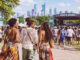 Stylish festivalgoers walk toward the Roots Picnic stage with the Philadelphia skyline in the background.