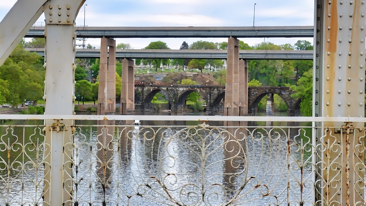 Ornate Falls Bridge railing frames a view of the Twin Bridges and historic stone railroad arches along the Schuylkill River in East Falls.