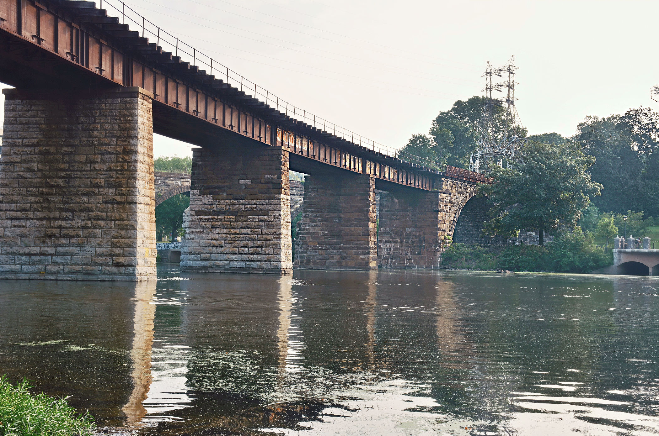 The Philadelphia and Reading Railroad Bridge curves across the Schuylkill River in East Falls, supported by stone piers and a single stone arch.