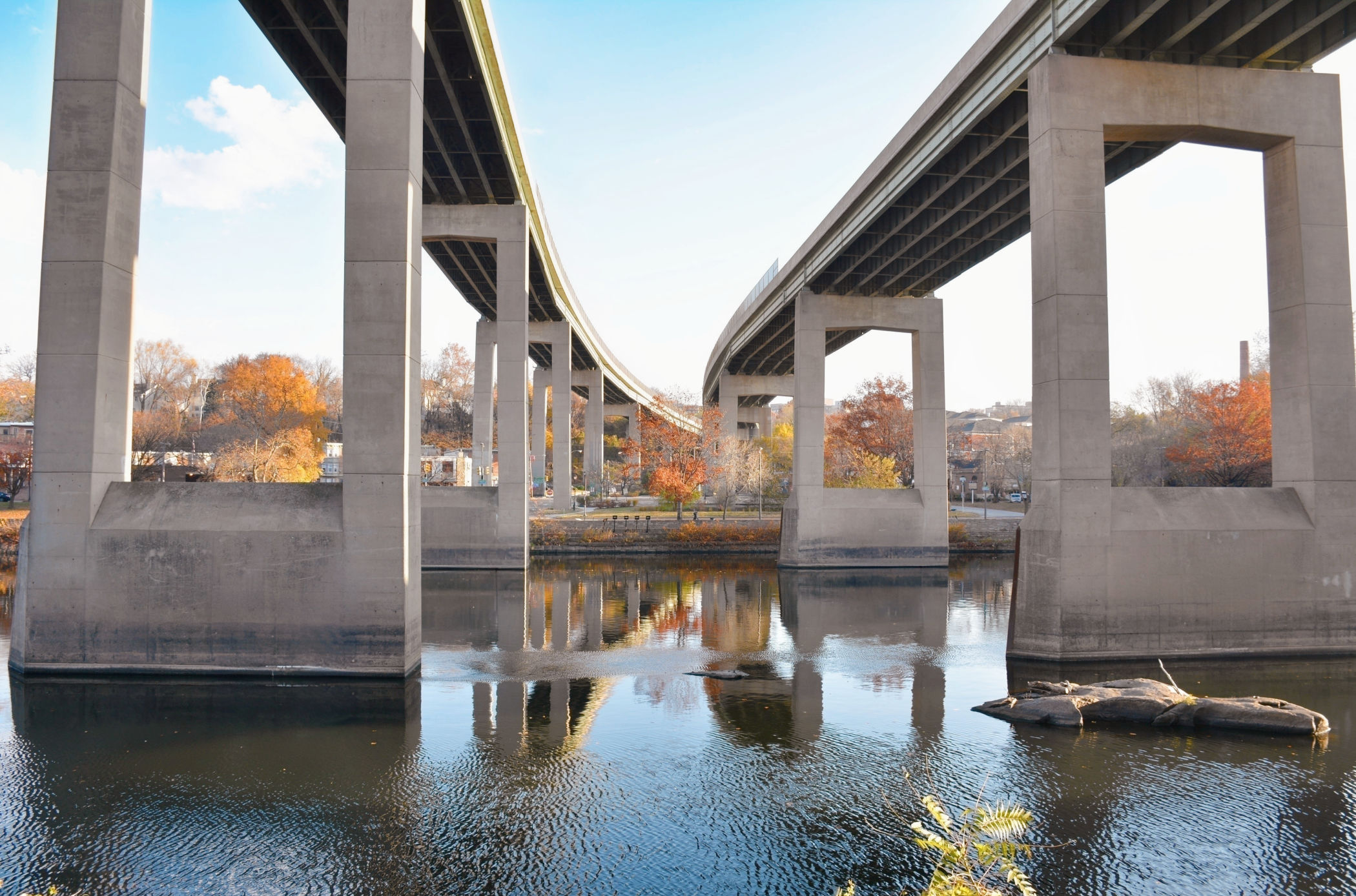 The Twin Bridges rise above the Schuylkill River in East Falls, with massive concrete piers framing autumn trees along the riverbank.