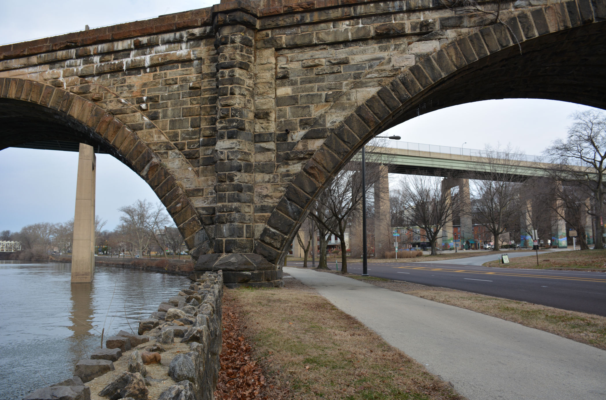 Stone arch of the Philadelphia & Reading Railroad Bridge along Kelly Drive in East Falls, with the Twin Bridges visible in the background.